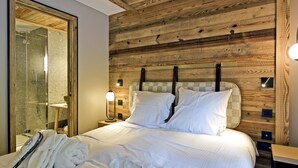 Ein Hotelzimmer mit hölzernem Kopfteil, einer Duschkabine aus Glas, einem Nachttisch mit Lampe und ordentlich gefalteten Handtüchern auf dem Bett.