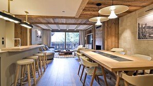 Eine moderne Küche mit Holzelementen, ein Essbereich mit langem Tisch und Stühlen sowie ein Blick ins Freie durch große Fenster.