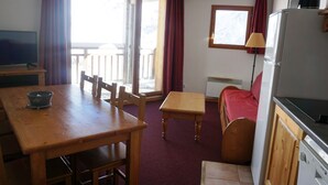 Una habitación pequeña con una mesa de comedor de madera, una cama individual, una kitchenette y un televisor.