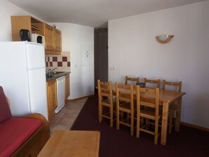 A compact kitchen with a refrigerator, microwave, and wooden cabinets. There is a dining table with chairs and a red sofa in the living area. - Modern Apartment for 6 with Balcony, Parking, and Free WiFi Near Slopes and Shops (Orcières Merlette)