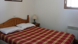 Una cama individual con colcha a cuadros, una mesita de noche con lámpara y un cuadro enmarcado en la pared.