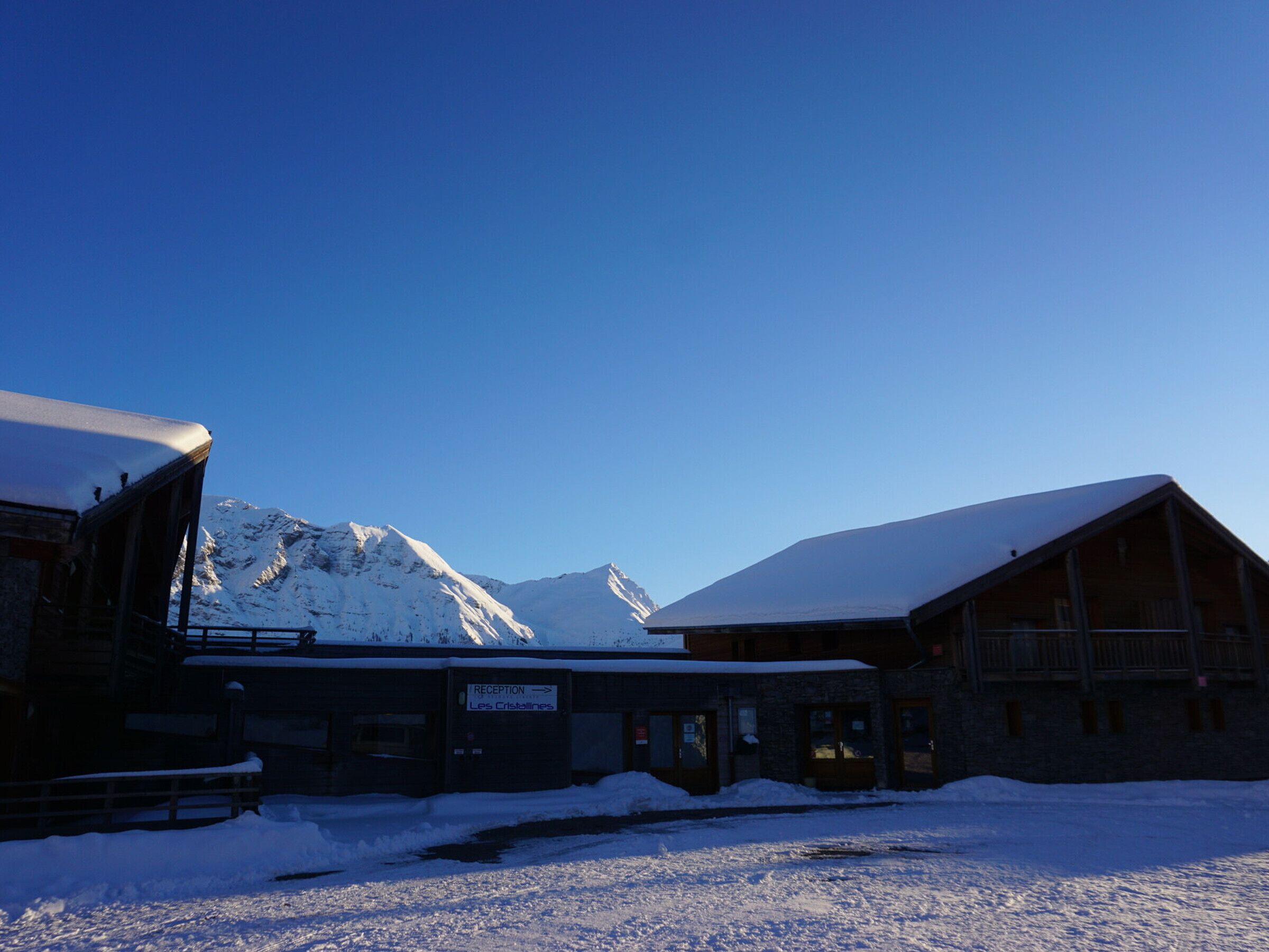 A snow-covered reception building with a sign indicating 'Les Cristallines' and a mountain backdrop.