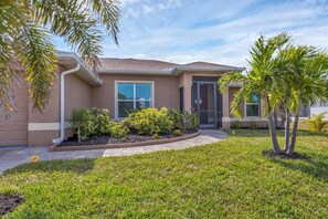 A residential house with a well-maintained lawn, a small garden with shrubs, and a palm tree.