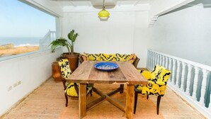 A balcony with a wooden table, yellow patterned chairs, a potted plant, and a view of the beach. - Private sea view house. (Essaouira)