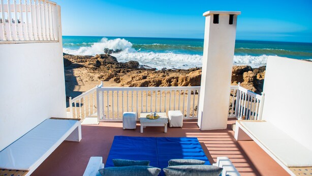 A balcony with a view of the ocean, featuring a white railing, a blue mat, and a small table with a tray. - Private sea view house. (Essaouira)