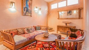 A cozy living room with a wooden sofa, a round coffee table, and a chair. There are wall-mounted lights and a large mirror above the sofa. - Private sea view house. (Essaouira)