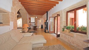 A cozy living room with a stone wall, wooden ceiling beams, a fireplace, and a view through a glass door. - Muralles - Central house with pool, air conditioning, and wifi in Alcúdia (Alcúdia)