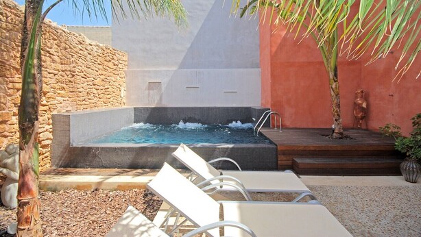 A spa area with a hot tub, white lounge chairs, and a stone wall. - Muralles - Central house with pool, air conditioning, and wifi in Alcúdia (Alcúdia)