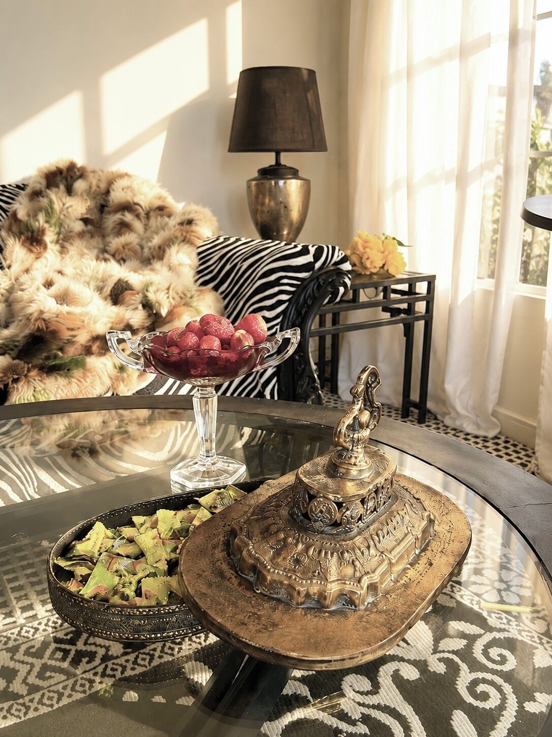 A room with a glass table, a decorative tray, a lamp, and a fur-covered chair.