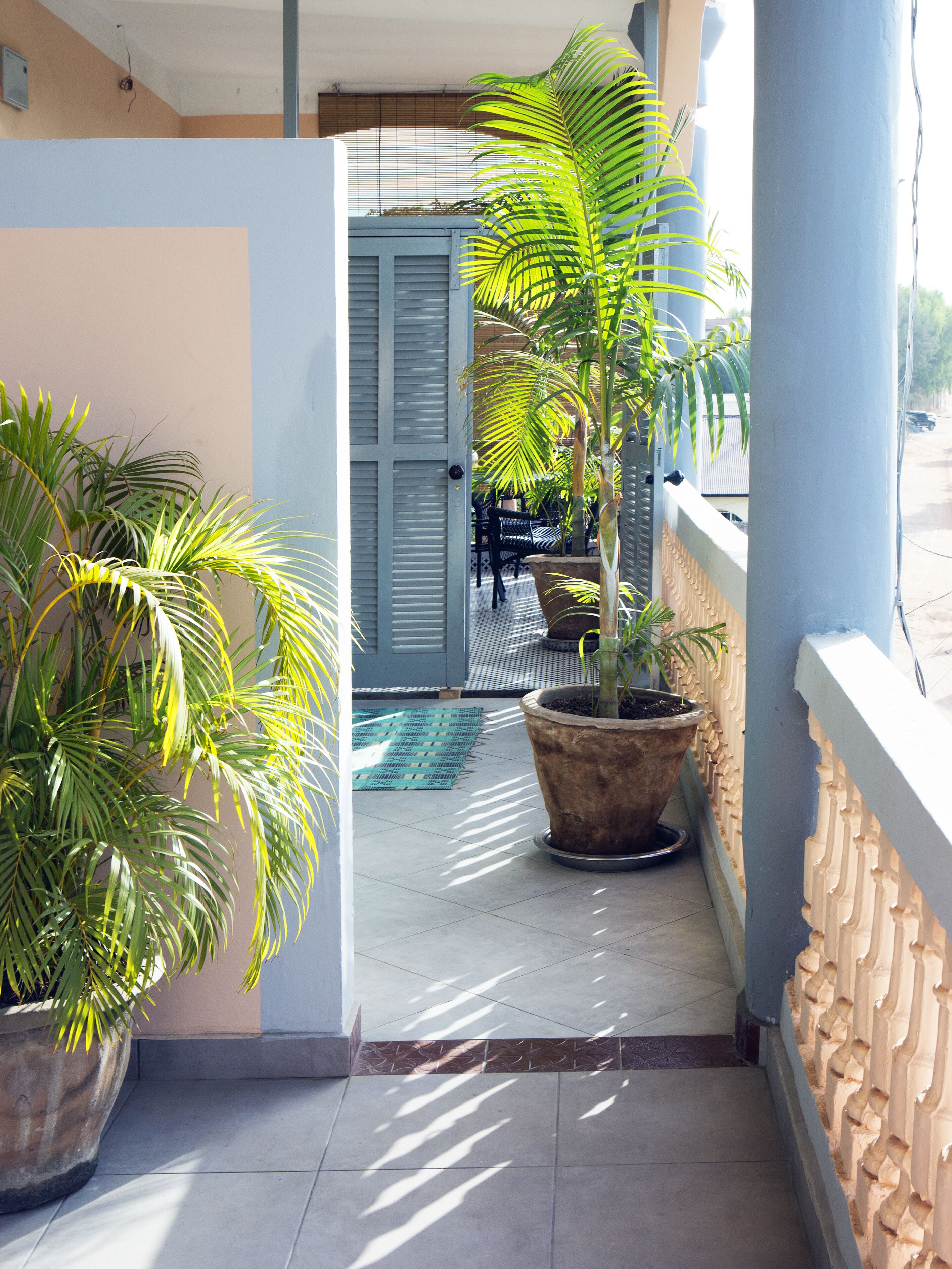 Un balcón estrecho con plantas en macetas, una puerta que da a un espacio cubierto y piso de baldosas.