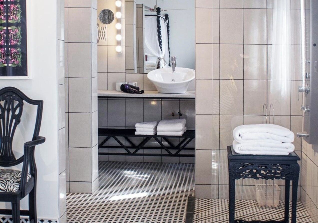 A bathroom with a white sink, a mirror with lights, a black chair, and a patterned floor.