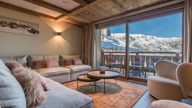 Un salón acogedor con un sofá, sillones y una mesa de centro. Un ventanal ofrece vistas a montañas nevadas.
