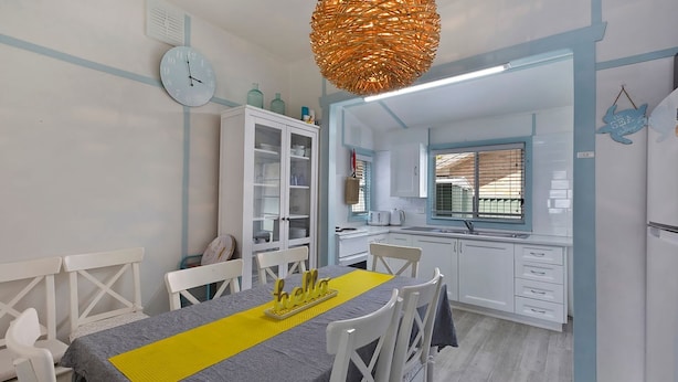 Una cocina compacta con armarios blancos, una mesa de comedor con sillas, un reloj y una lámpara colgante original.