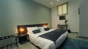 Quarto moderno com uma cama grande, mesas de cabeceira, um criado-mudo, uma janela e uma pequena mesa com um vaso.