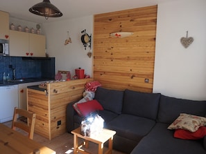 En hyggelig stue med trævæg, sofa, lille bord og et køkkenområde med skabe og vask.
