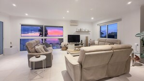 A modern living room with a sofa, armchair, and a flat-screen TV. - Villa Acacia- Spectacular Ocean view & heated pool (Arco Da Calheta)