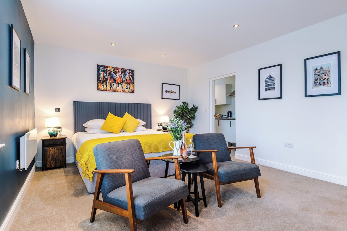 A modern bedroom with a bed, two armchairs, a small table, and a nightstand.