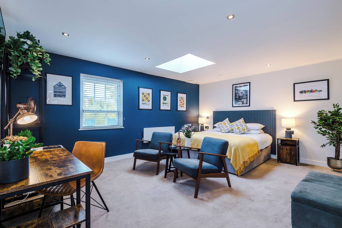 A modern bedroom with a bed, two chairs, a table, and a potted plant.
