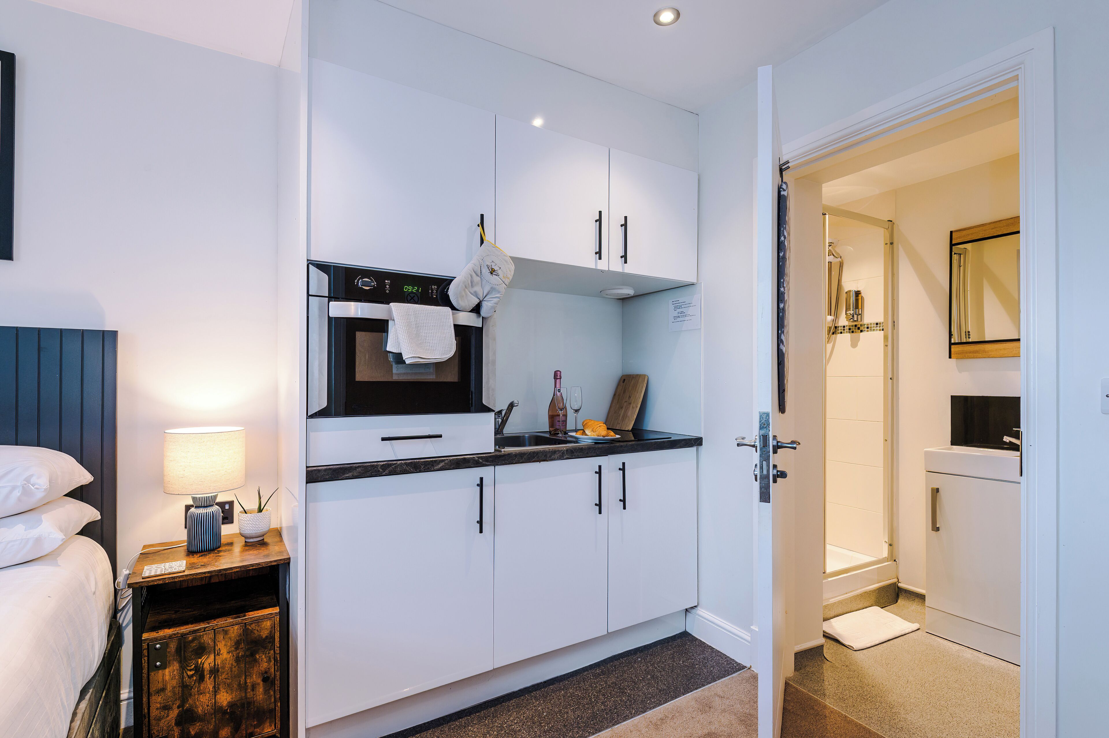 A compact kitchen with white cabinets, a built-in oven, and a countertop with a kettle and wine glass.