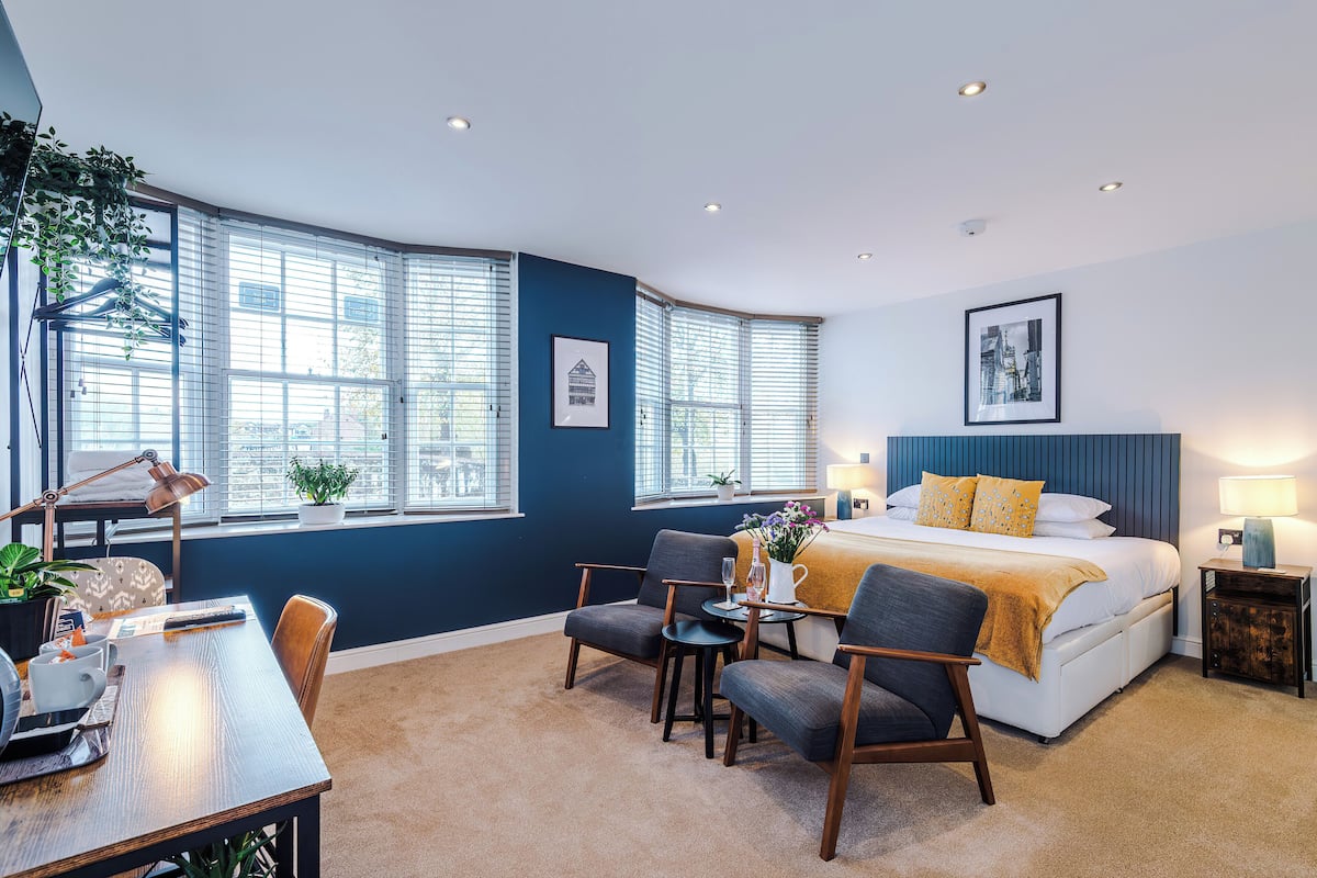A modern bedroom with a curved ceiling, large windows, a bed with a headboard, bedside tables, and a desk with a chair.