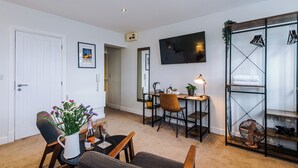 A living room with a white door, a TV mounted on the wall, a dining table with chairs, a sofa, and a fan. - Deva Leisure (Chester)
