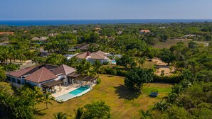 An aerial view of a residential area with houses, a swimming pool, and a view of the ocean. - Villa for private events (La Romana)