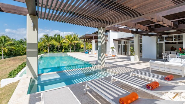 A modern outdoor pool area with a pergola, lounge chairs, and a view of the surrounding landscape. - Villa for private events (La Romana)