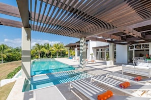 A modern outdoor pool area with a pergola, lounge chairs, and a view of the surrounding landscape. - Villa for private events (La Romana)