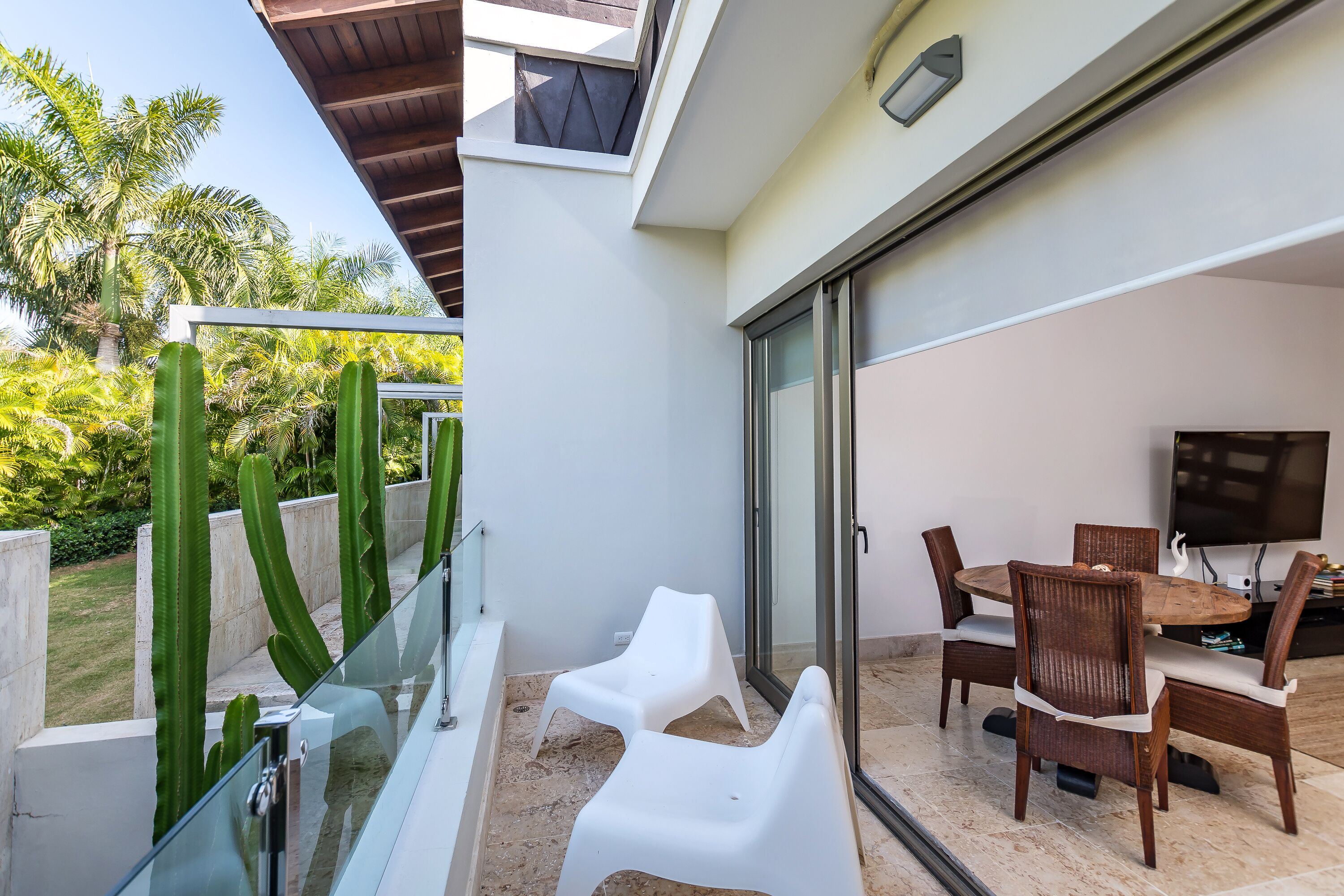 Un área de comedor exterior moderna con barandilla de vidrio, una piscina y vistas a palmeras.