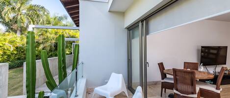 Un área de comedor exterior moderna con barandilla de vidrio, una piscina y vistas a palmeras.