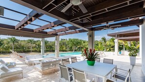 A covered outdoor area with a pool, lounge chairs, and a dining table. - Villa for private events (La Romana)