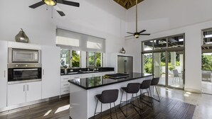 A modern kitchen with a central island, bar stools, and a ceiling fan. - Villa for private events (La Romana)