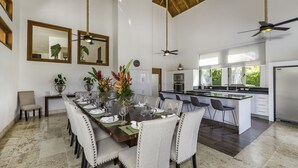 A spacious dining area with a long table set for a meal, a kitchen with a large island, and a ceiling fan. - Villa for private events (La Romana)