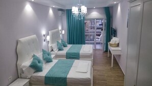 A hotel room with two beds, teal bedding, a chandelier, a small table with a basket, and a view of the balcony. - Apartments Flower Residence (Sarandë)
