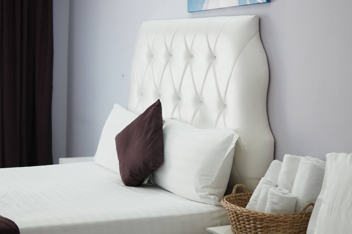 A hotel room with two beds, a large white headboard, a wall-mounted artwork, and a wicker basket on the nightstand.