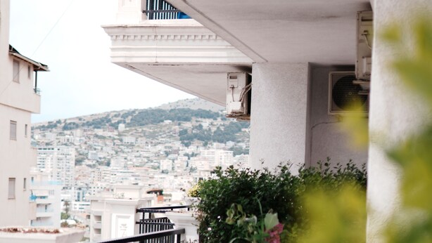 A balcony with a white railing, a table with chairs, and a potted plant. - Apartments Flower Residence (Sarandë)