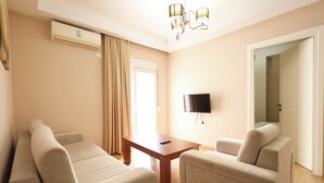 A living room with a sofa set, a TV mounted on the wall, and an air conditioning unit. - Apartments Flower Residence (Sarandë)