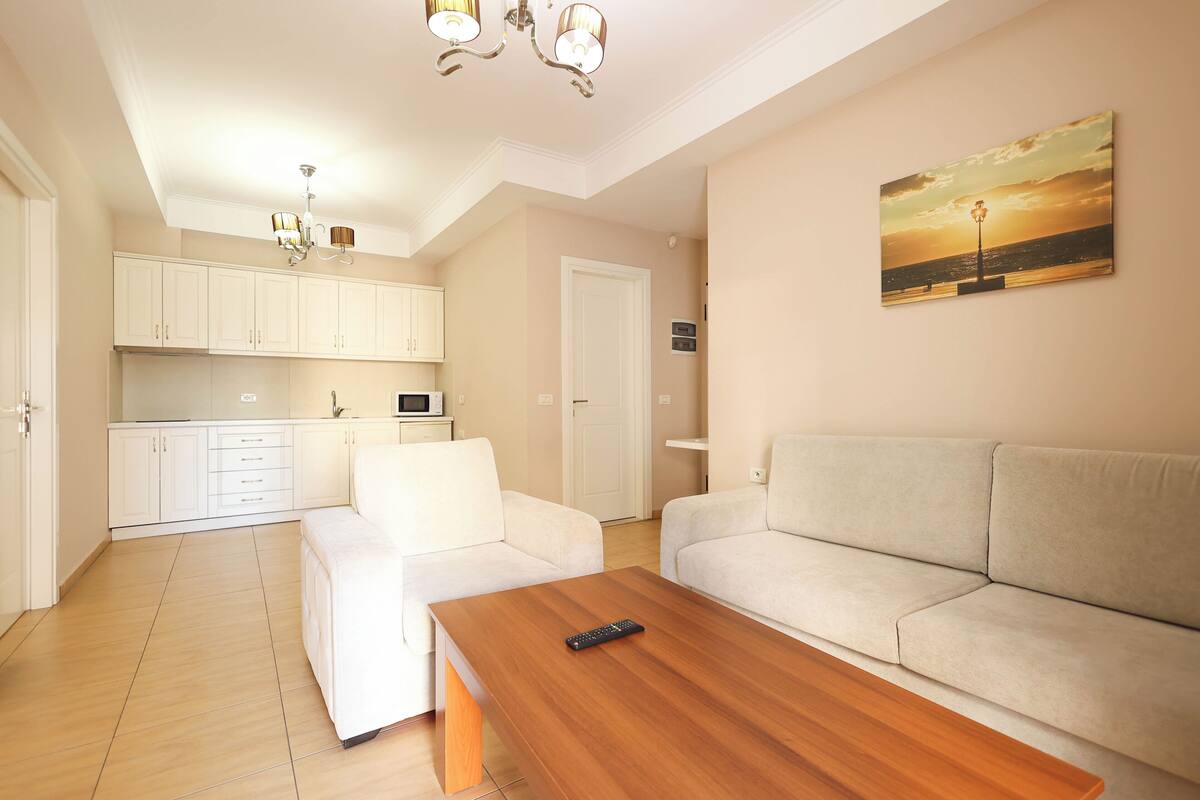 A modern living room with a wooden coffee table, a beige sofa, and a kitchen in the background.