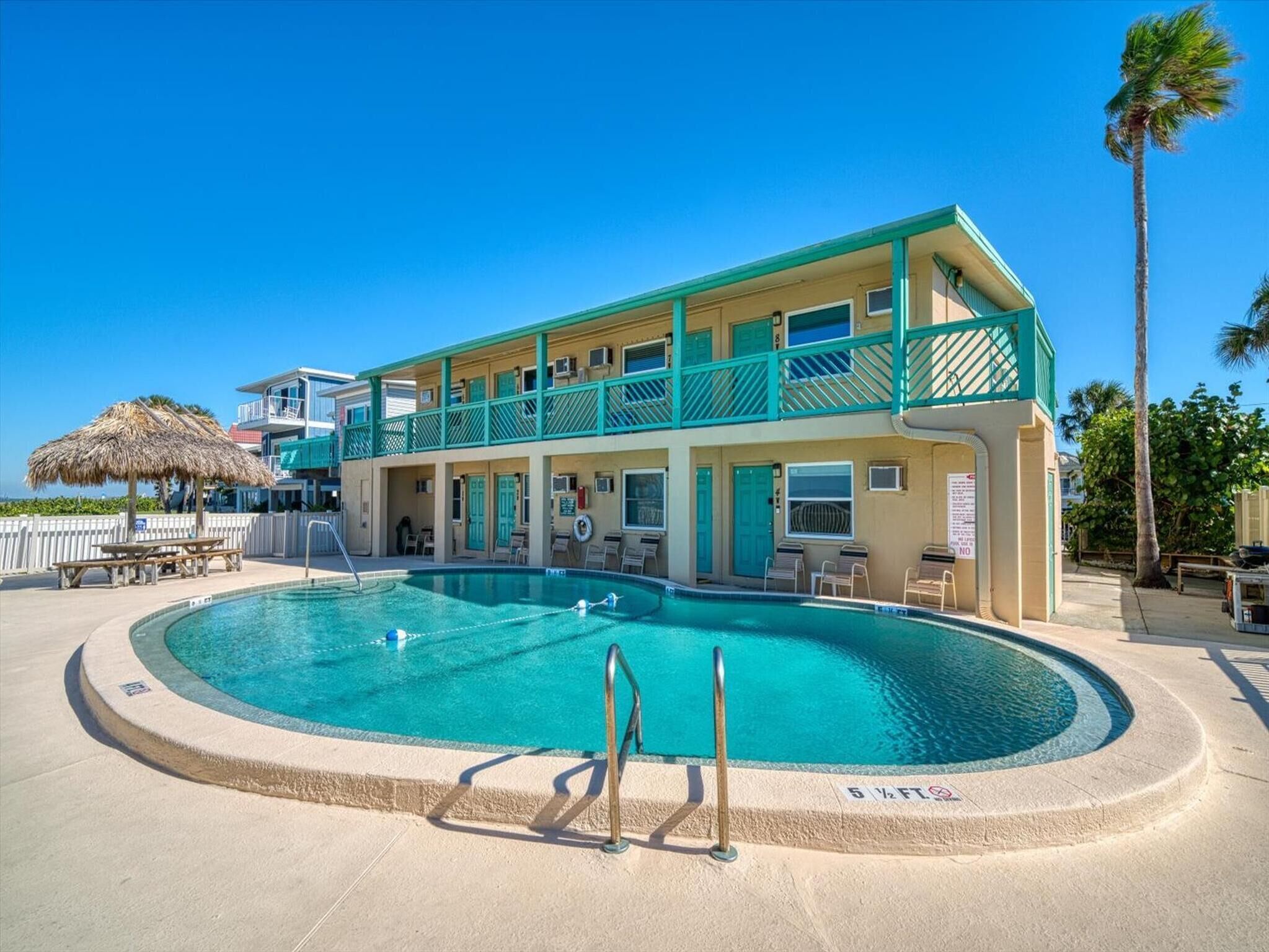 Ein zweistöckiges Hotel mit Pool, Außenbereich und Sonnenschirm mit Strohdach.