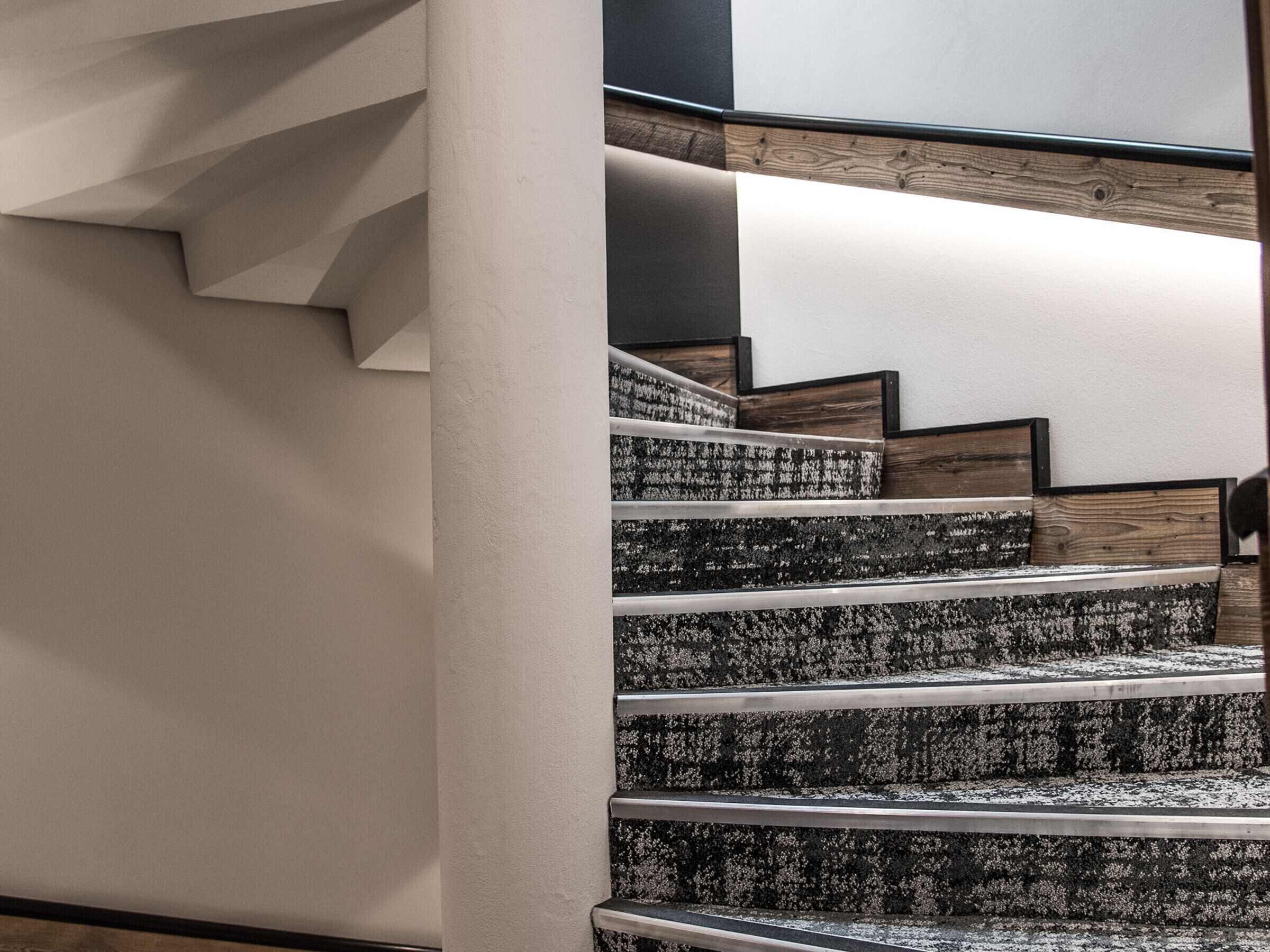 A staircase with a modern design, featuring a combination of carpeted steps and wooden elements.