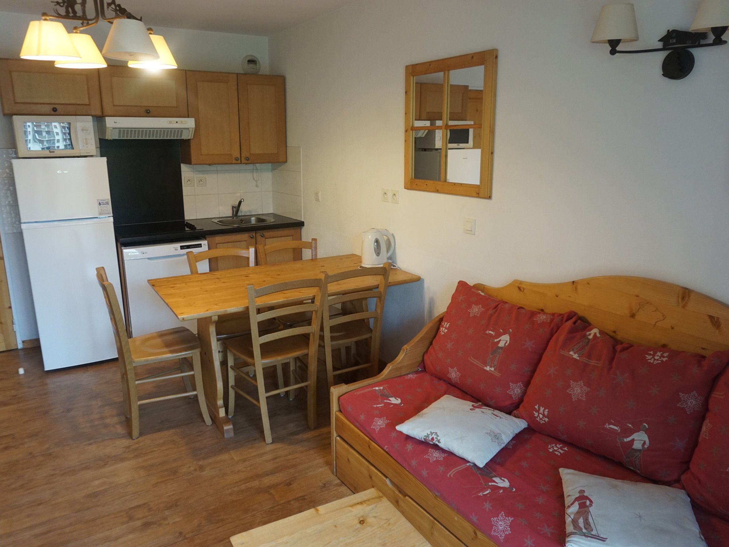 A compact living space with a kitchenette, a dining table with chairs, and a sofa with patterned cushions.
