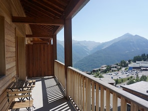 A wooden balcony with a view of a mountain range and a parking lot below.