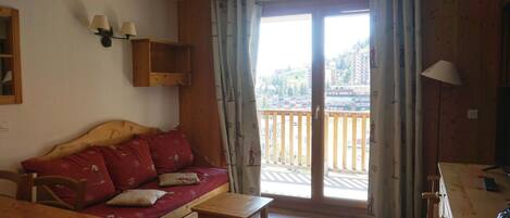 A cozy living room with a wooden sofa, a small table, and a balcony with a view of buildings.
