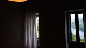 A room with a window overlooking a river and greenery, a hanging lamp, and a curtain partially drawn.