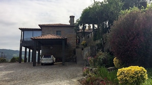 A stone house with a car parked in front, surrounded by greenery and a cobblestone driveway.