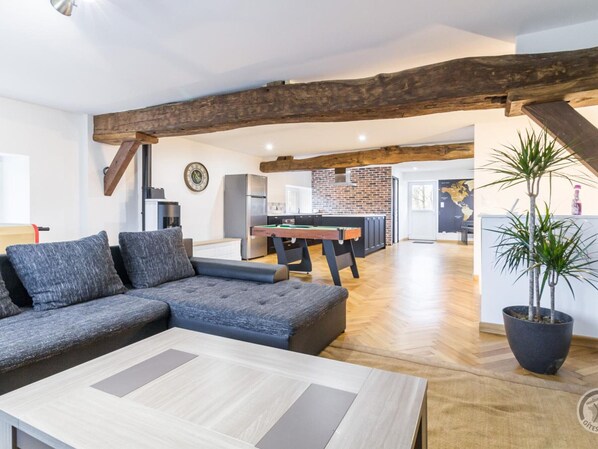 A modern living room with a sectional sofa, a pool table, and a wooden ceiling beam.