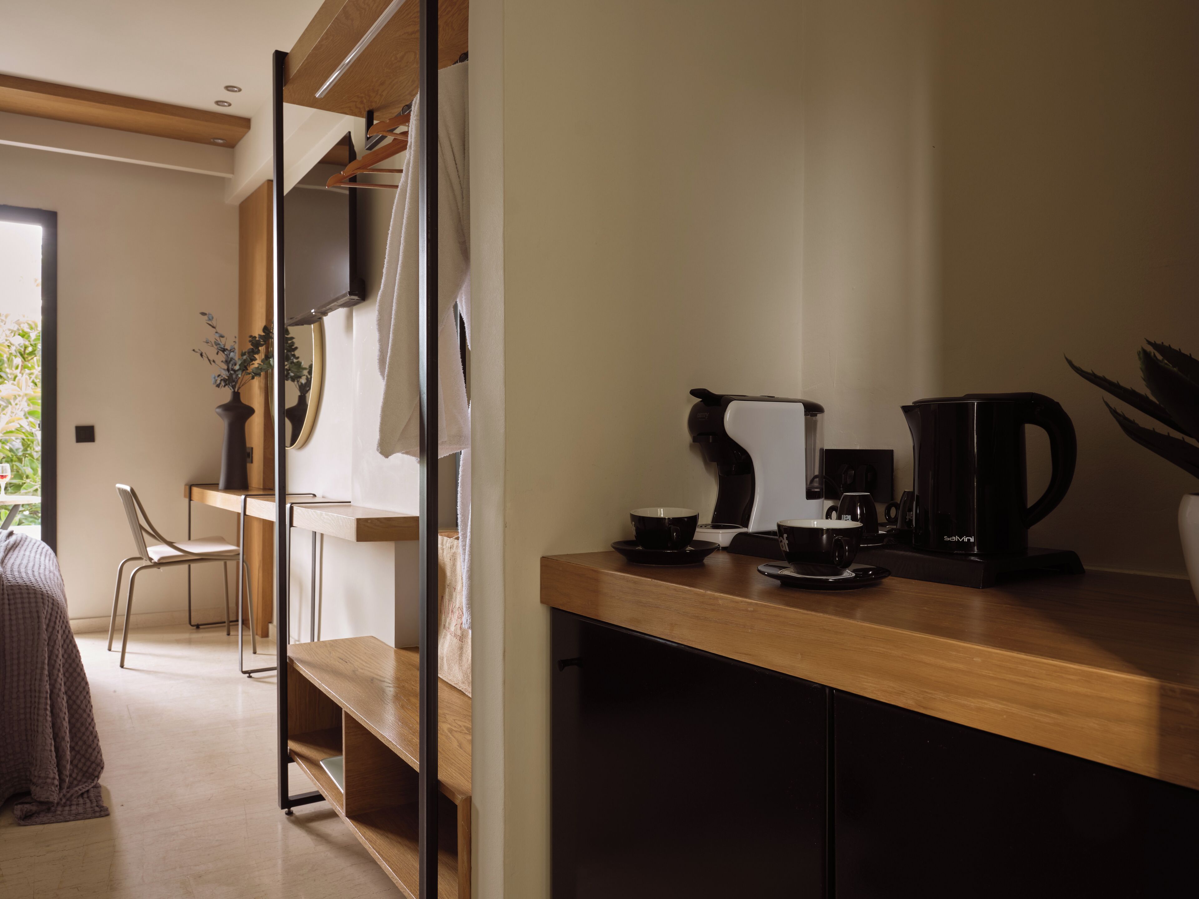 A modern kitchen with a wooden countertop, a coffee maker, and a kettle. There is a chair and a dining table in the background.