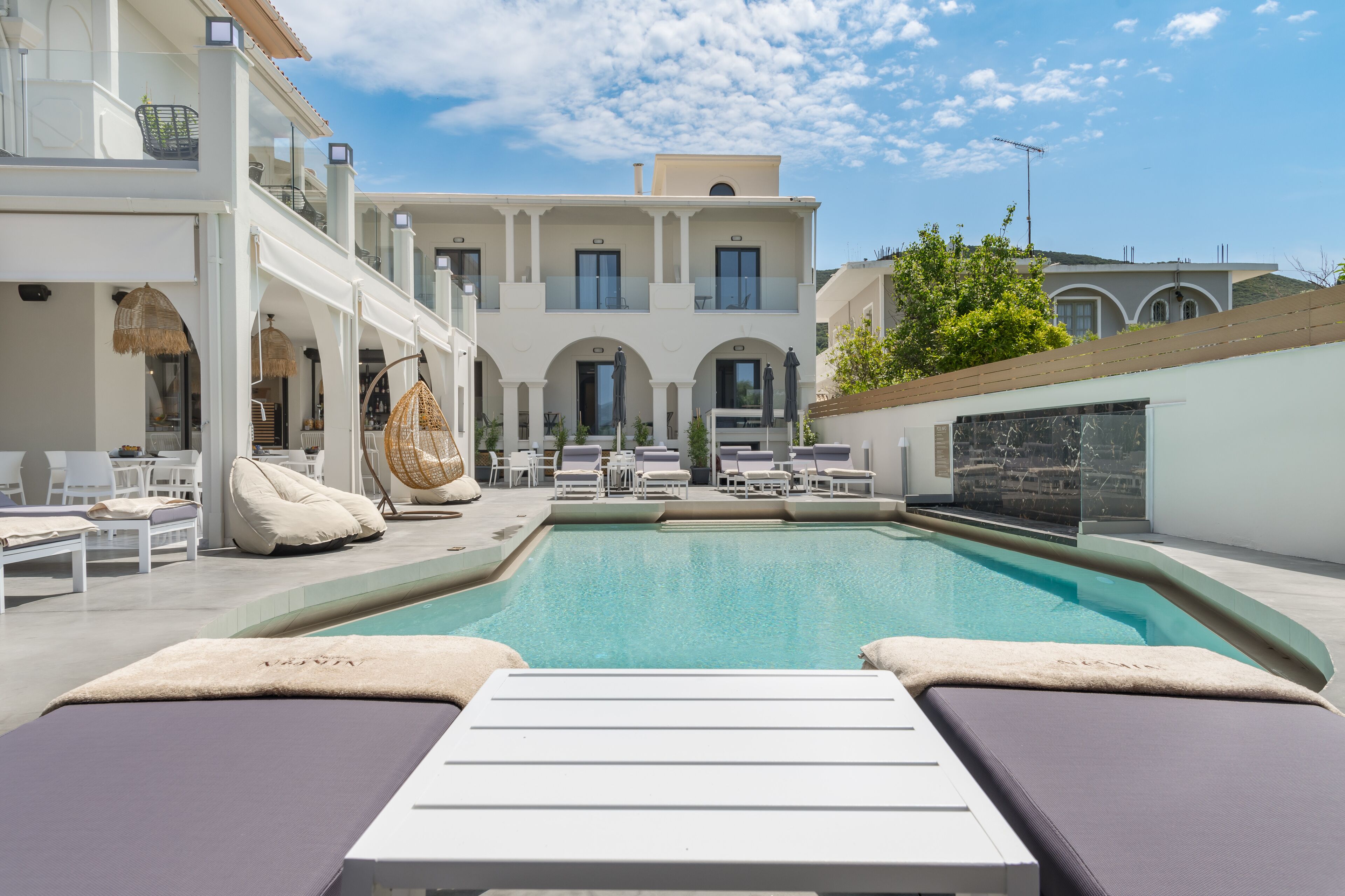 A rooftop pool area with lounge chairs, a swimming pool, and a building with multiple balconies.