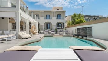 A rooftop pool area with lounge chairs, a swimming pool, and a building with multiple balconies.