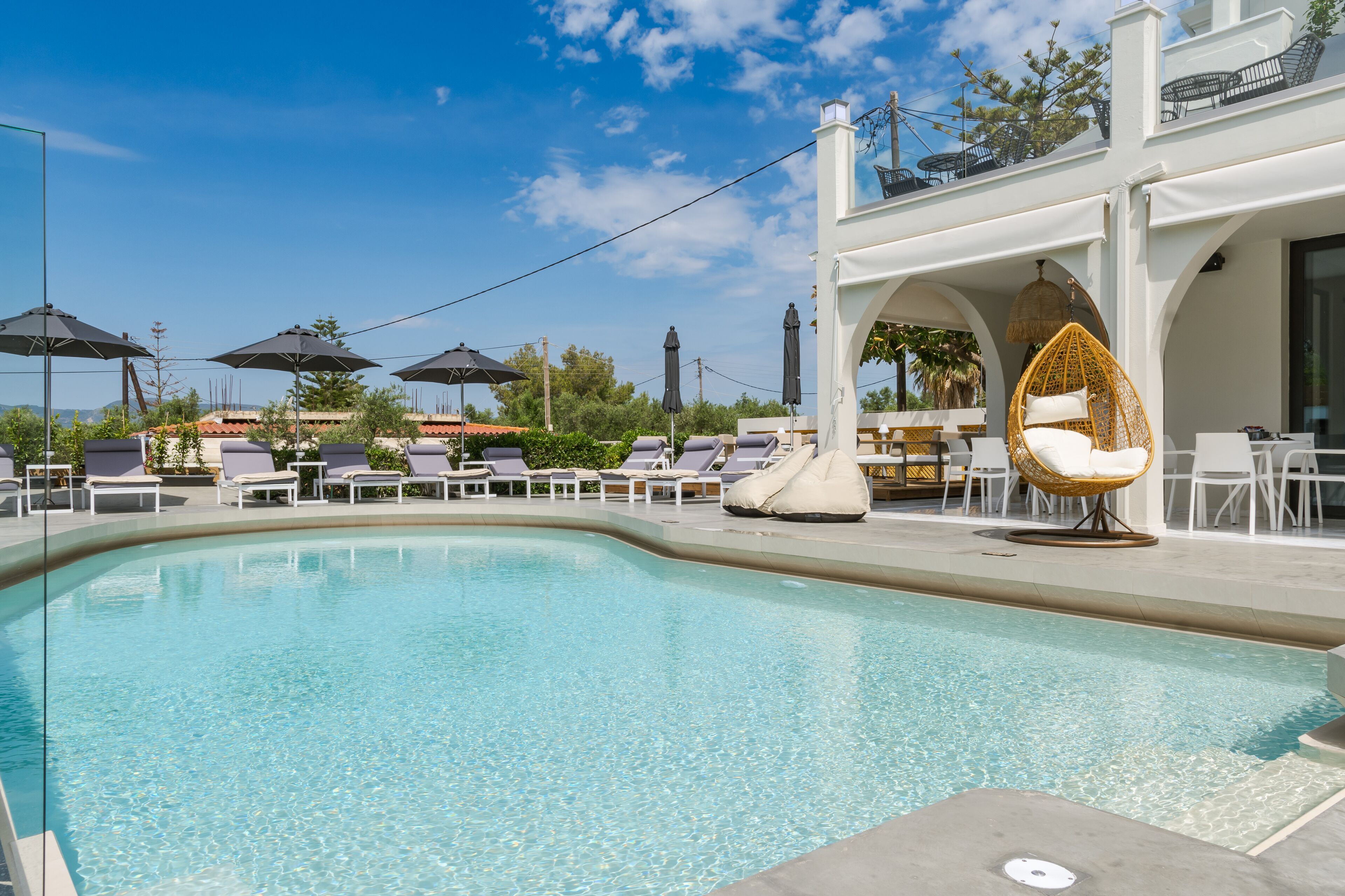A pool area with lounge chairs, umbrellas, and a white building with outdoor seating.